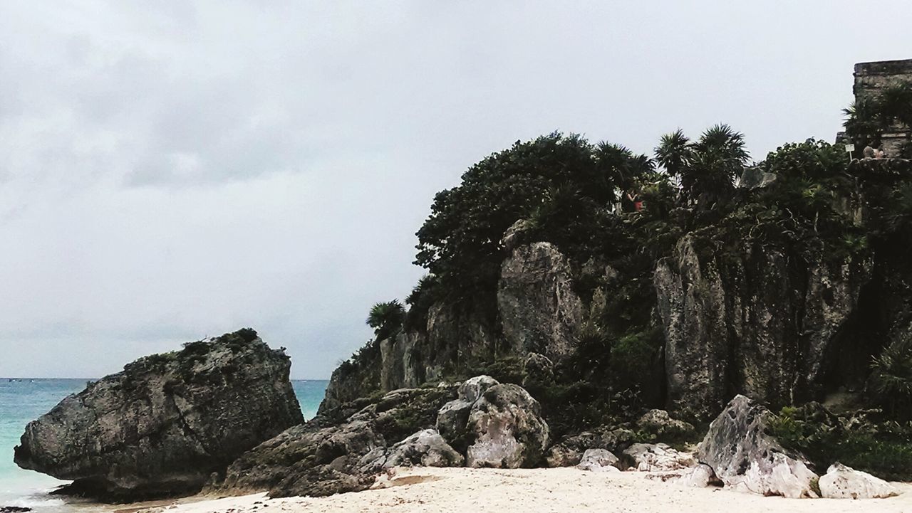 Rock formations by sea against cloudy sky