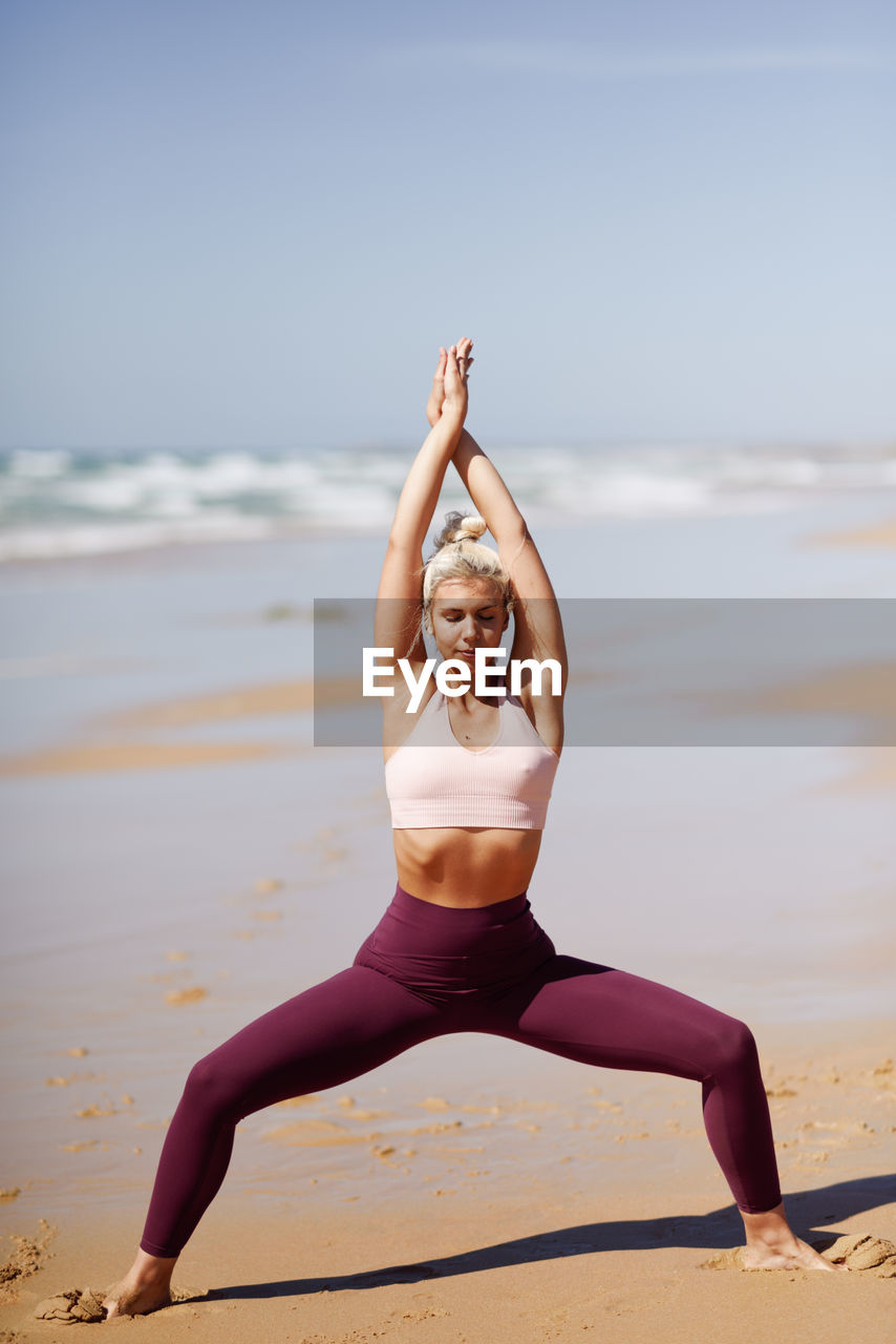 Full length of young woman exercising at beach on sunny day