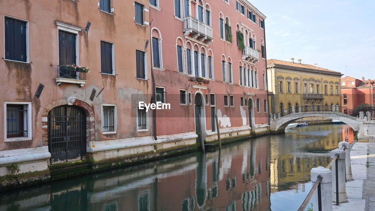 Canal by buildings in city against sky