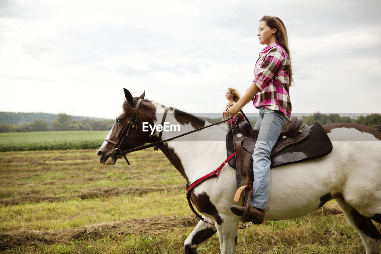 Side view of cowgirls riding on horse