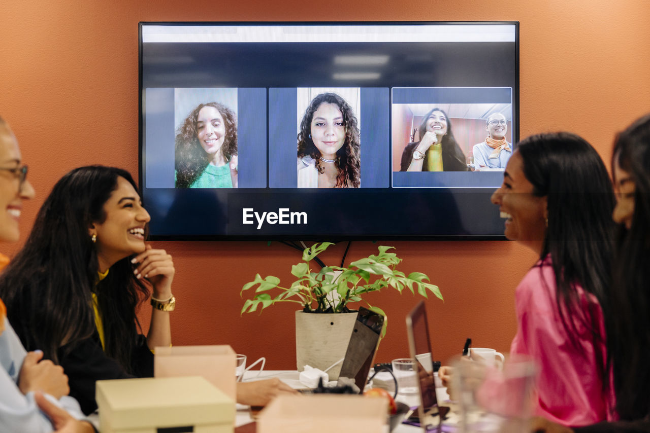 Happy female entrepreneurs discussing during video call at office