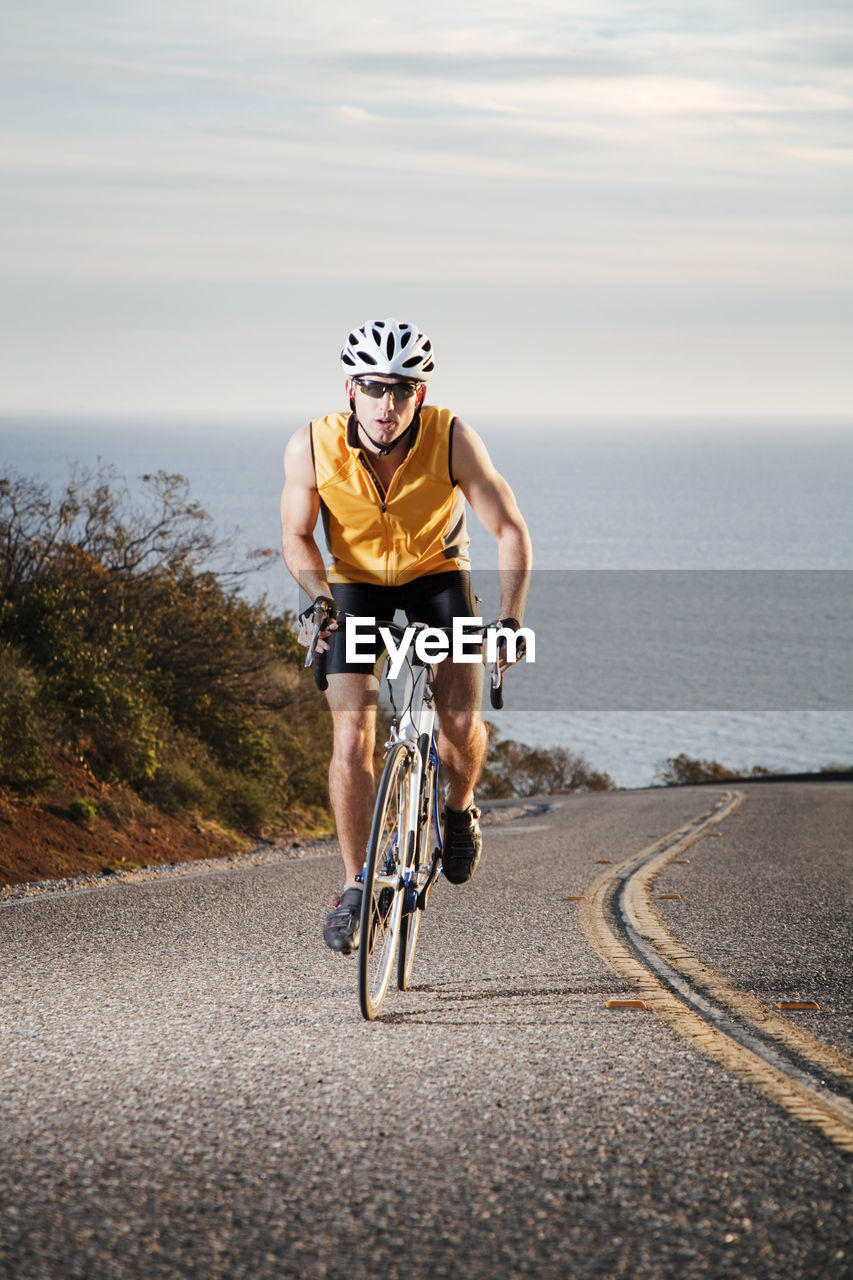 Man cycling on road against sea