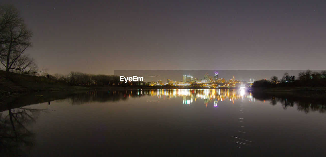 River by illuminated trees against sky at night