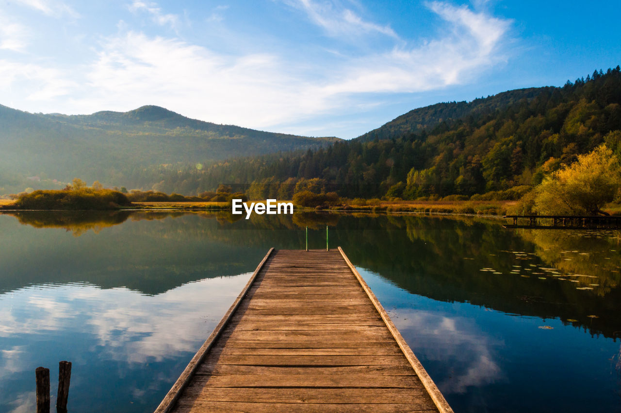 Pier by calm lake against sky during autumn