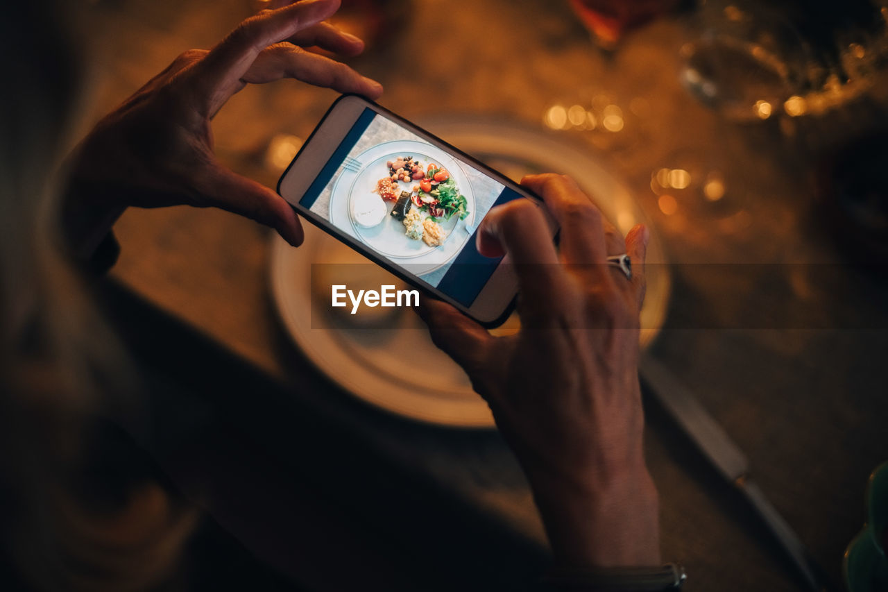 High angle view of mature woman photographing food at dining table in dinner party