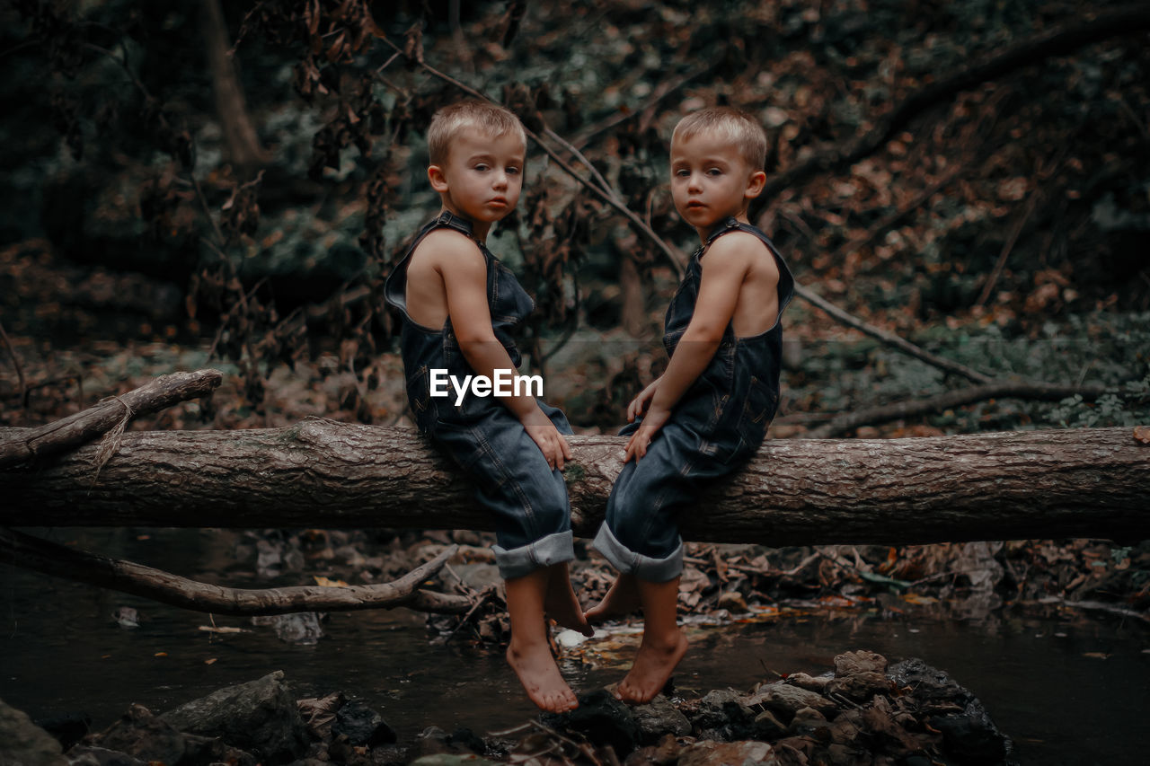 Full length of twin siblings sitting on wood