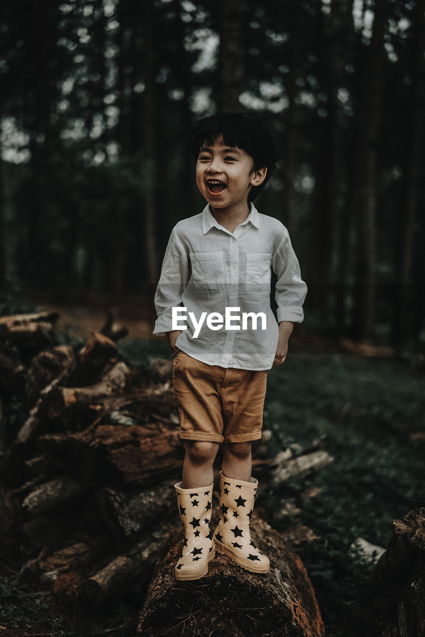 Happy boy with mouth open standing on wood in forest