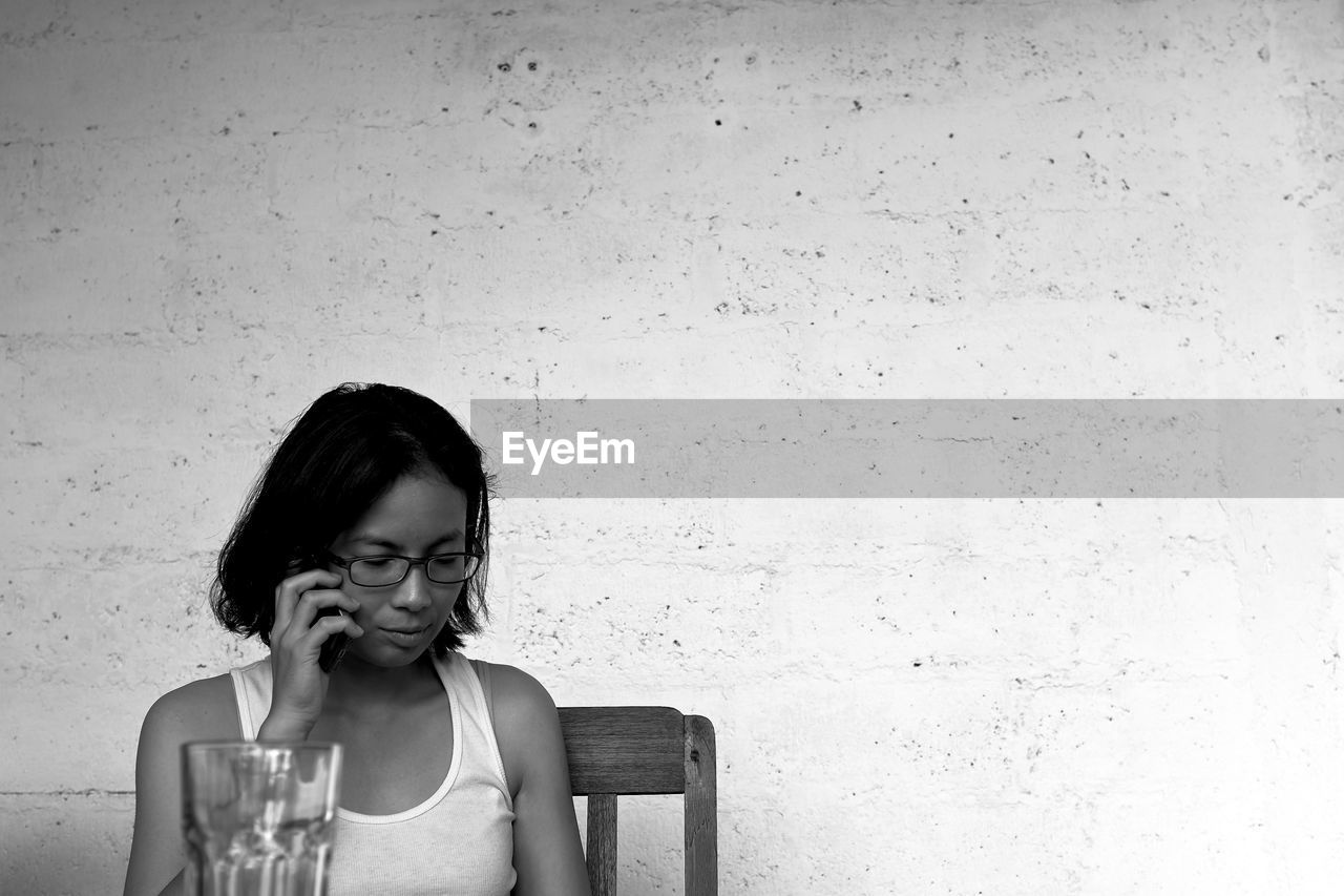 Young woman talking on mobile phone while sitting against wall