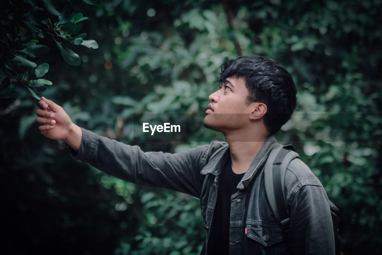 Young man looking away while standing against plants