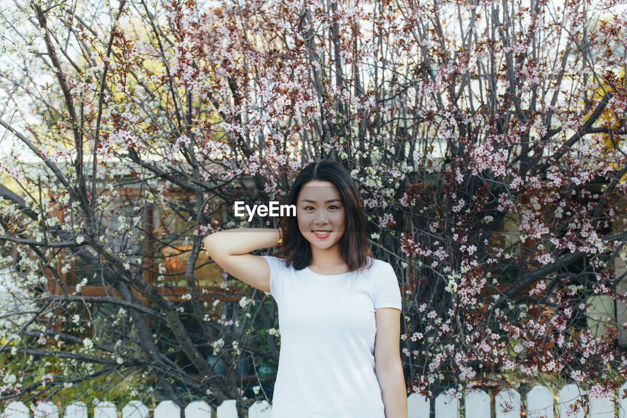 Portrait of smiling young woman standing against trees