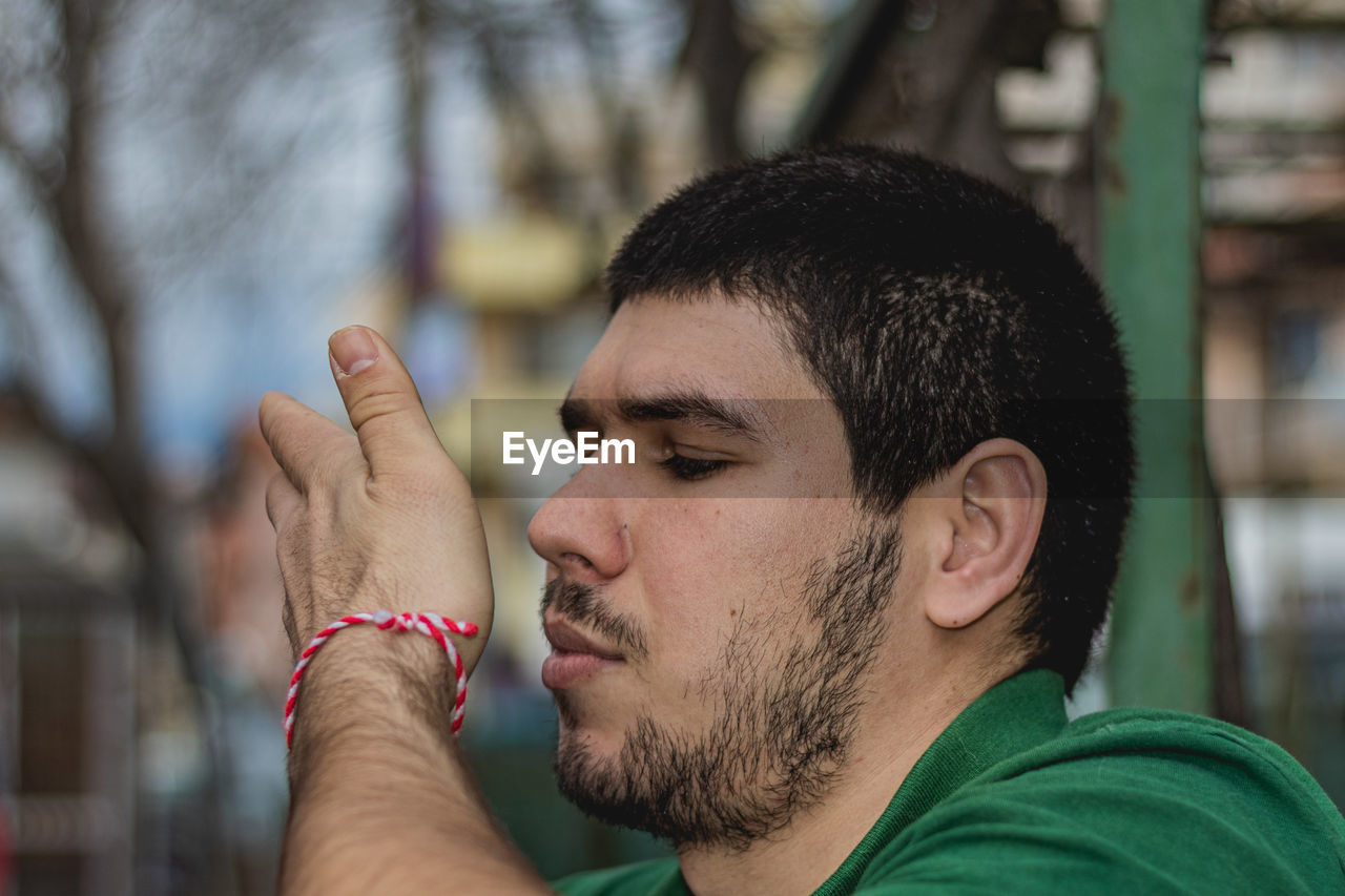 CLOSE-UP OF YOUNG MAN LOOKING AWAY OUTDOORS