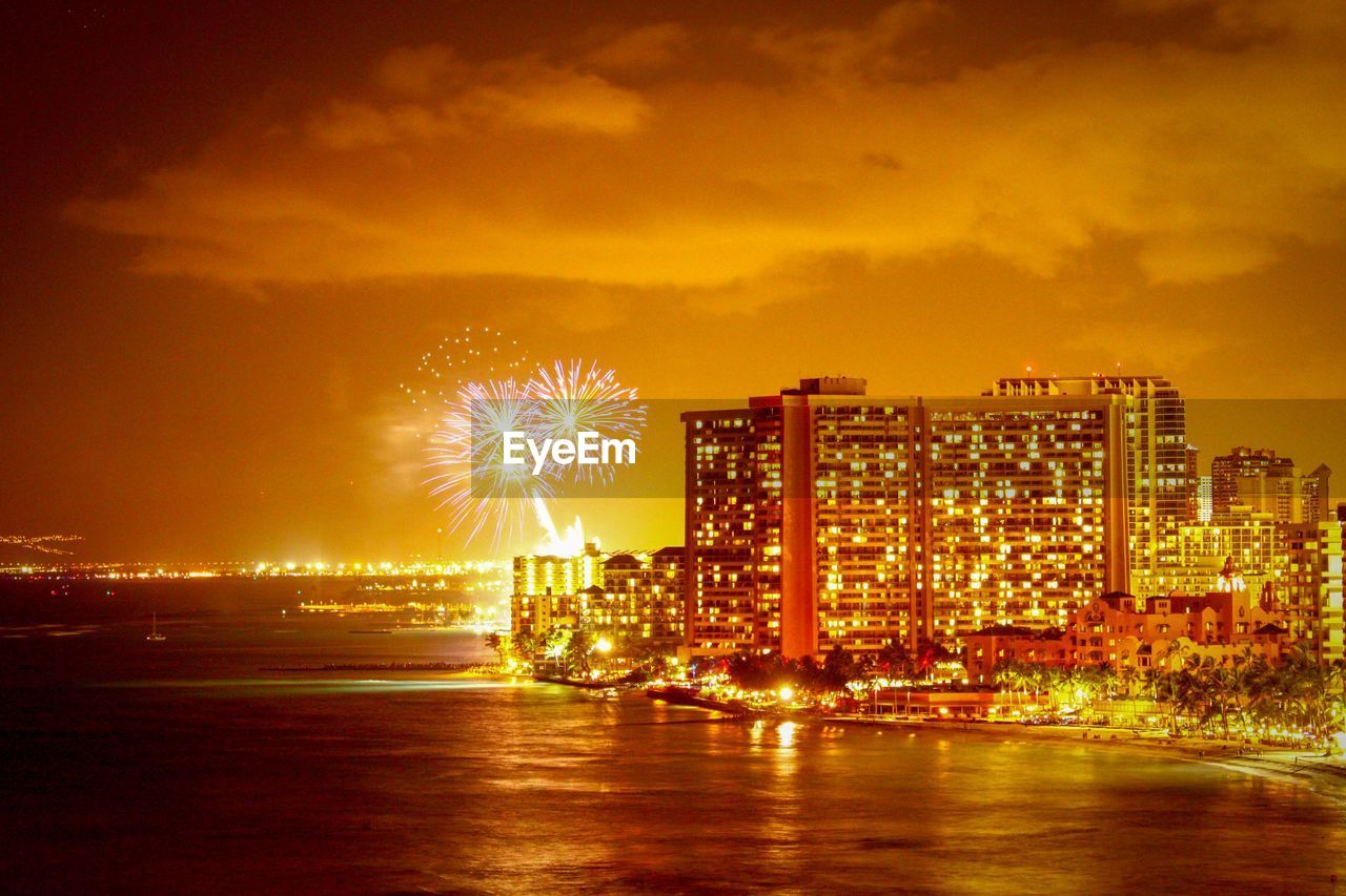 FIREWORK DISPLAY OVER ILLUMINATED CITYSCAPE AGAINST SKY