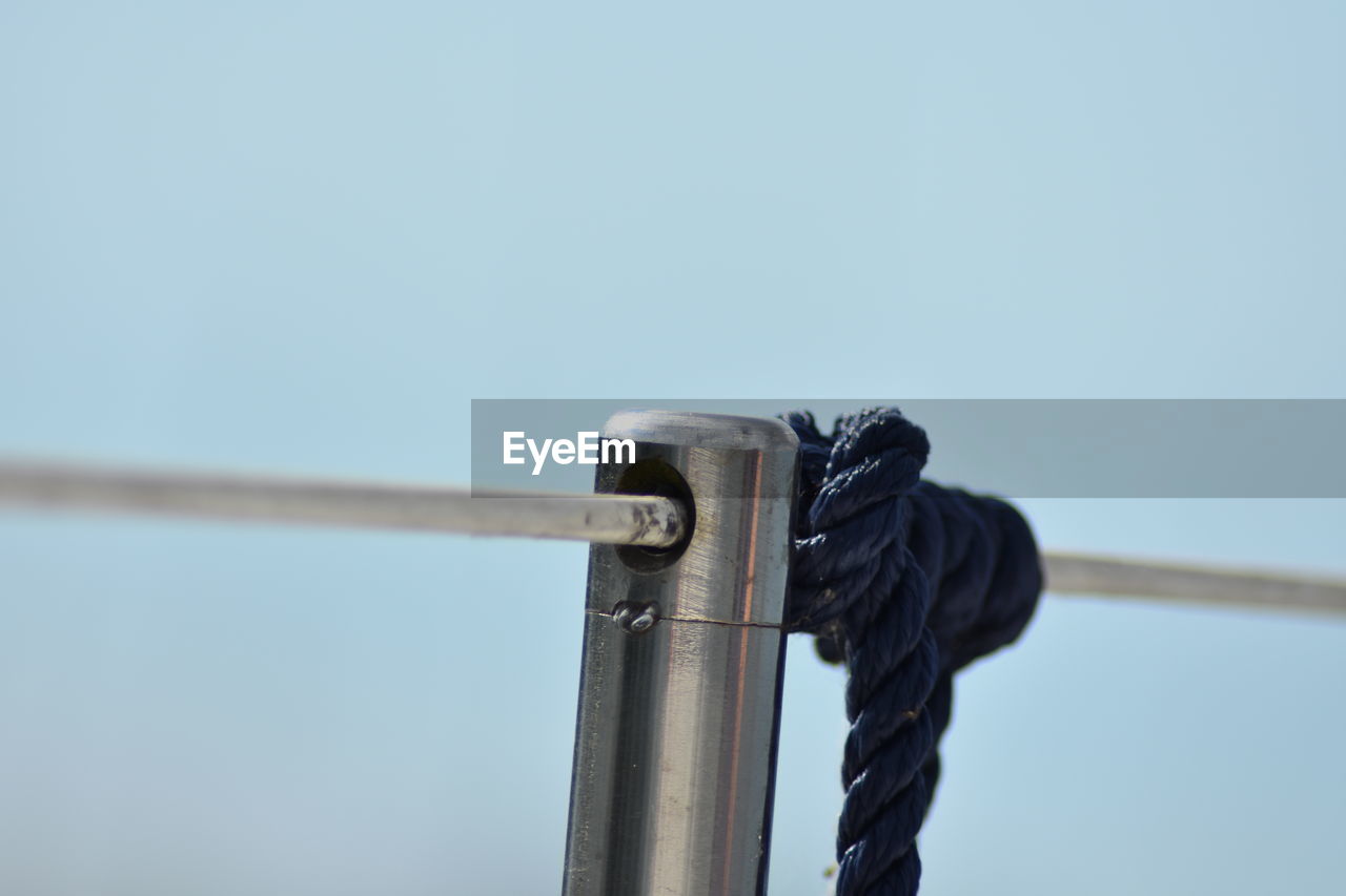 CLOSE-UP OF ROPE TIED TO METAL AGAINST SKY