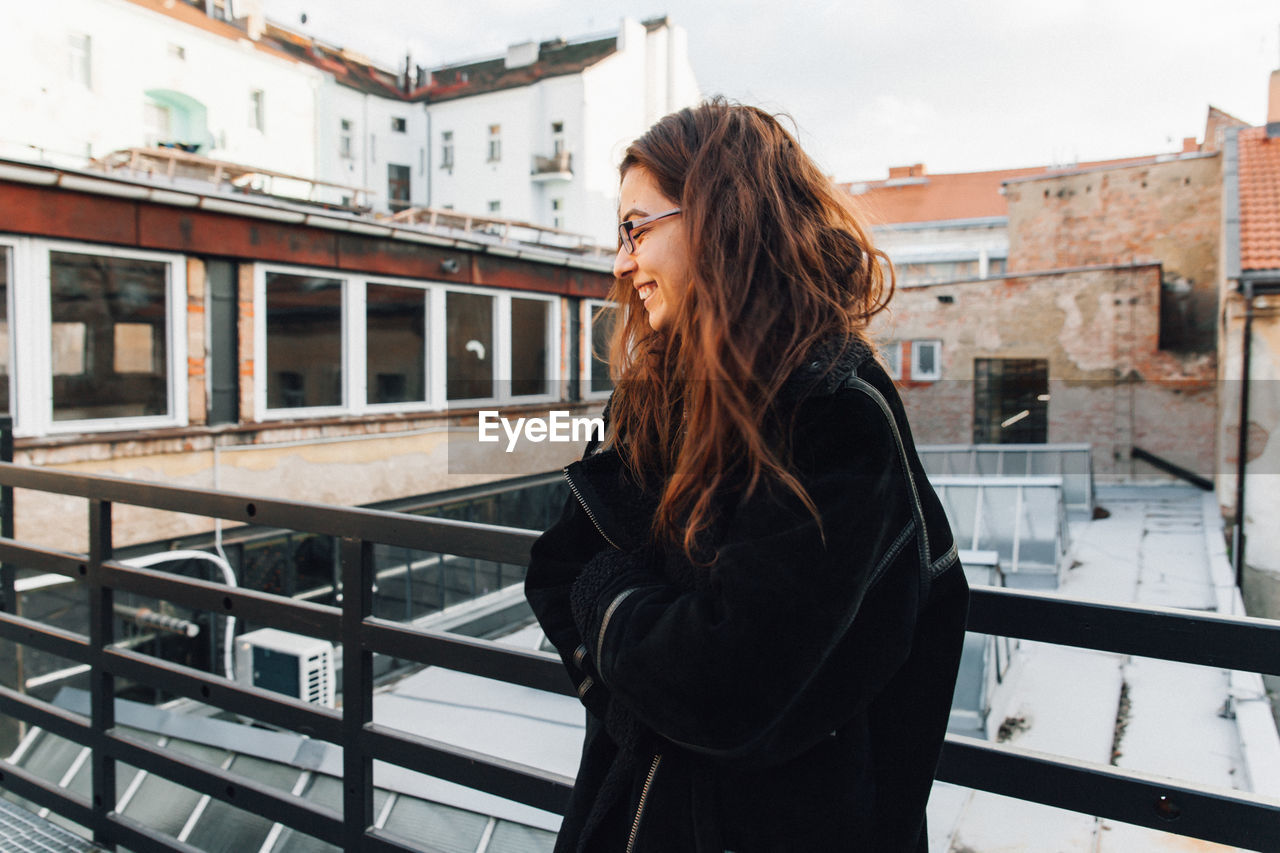 Smiling young woman standing by railing during winter