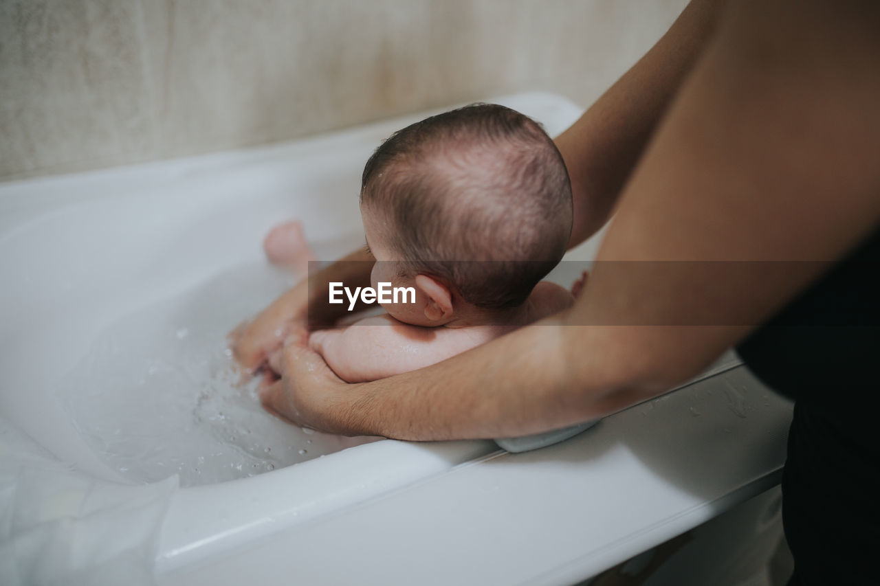 Midsection of mother bathing toddler in bathtub