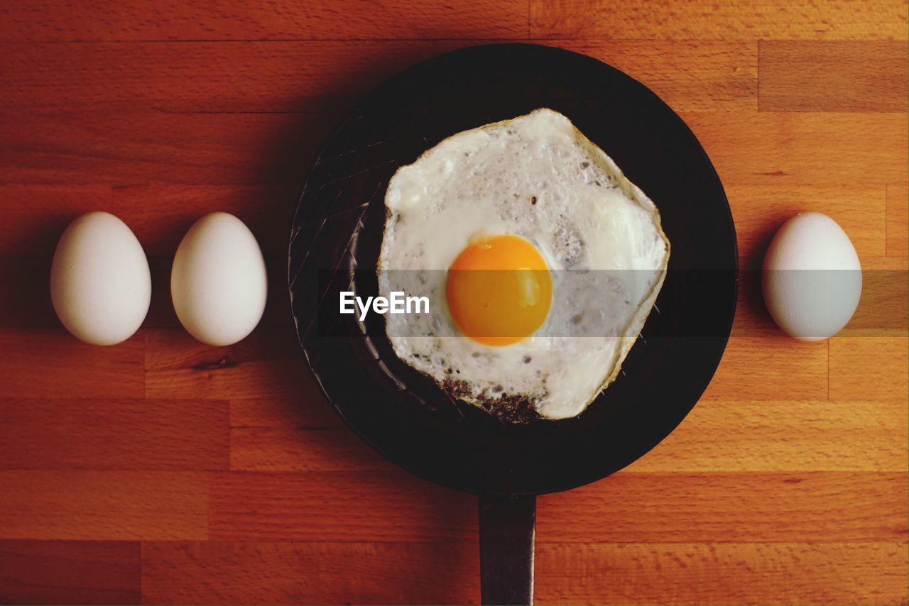 Directly above shot of eggs and fried egg in frying pan on table