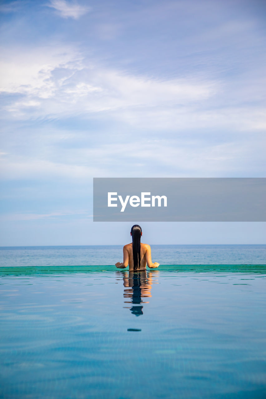 Rear view of woman in infinity pool against sky