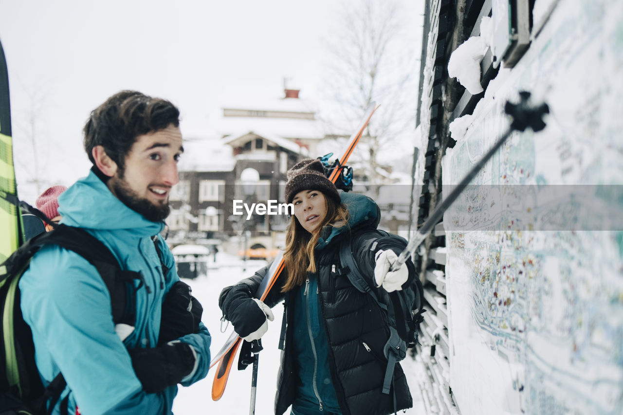 Man standing by confident woman pointing at map with ski pole