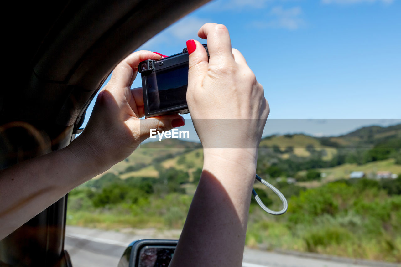 Cropped hand of woman photographing through car