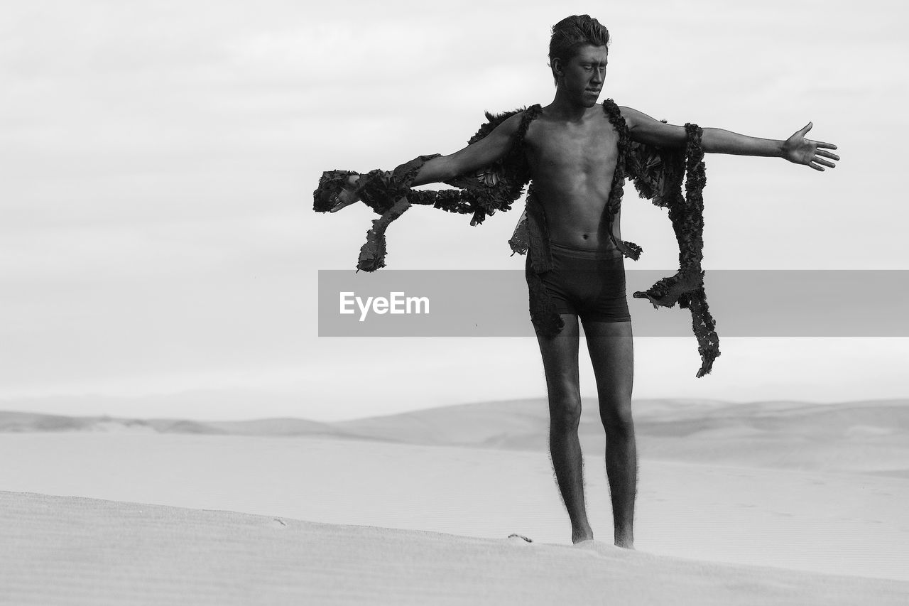 Model with costume wing standing at sandy desert against sky