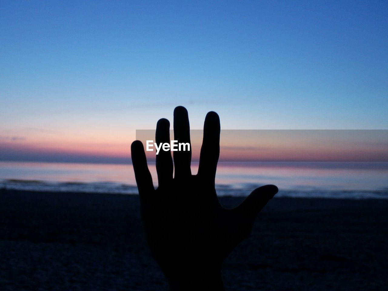 CLOSE-UP OF SILHOUETTE HAND AGAINST SEA