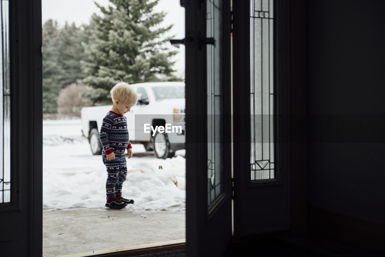 Side view of baby boy standing on snow seen through doorway