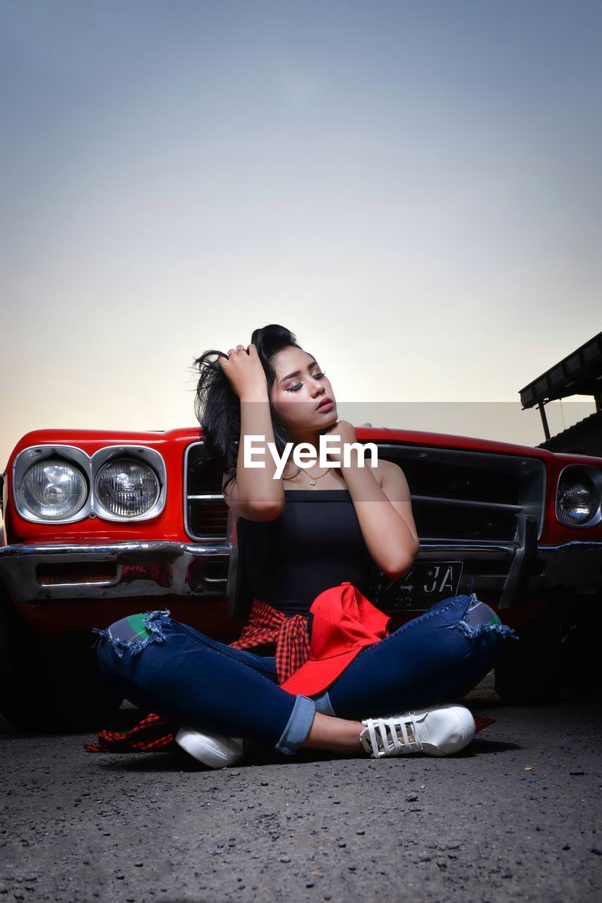 Woman sitting on car against sky