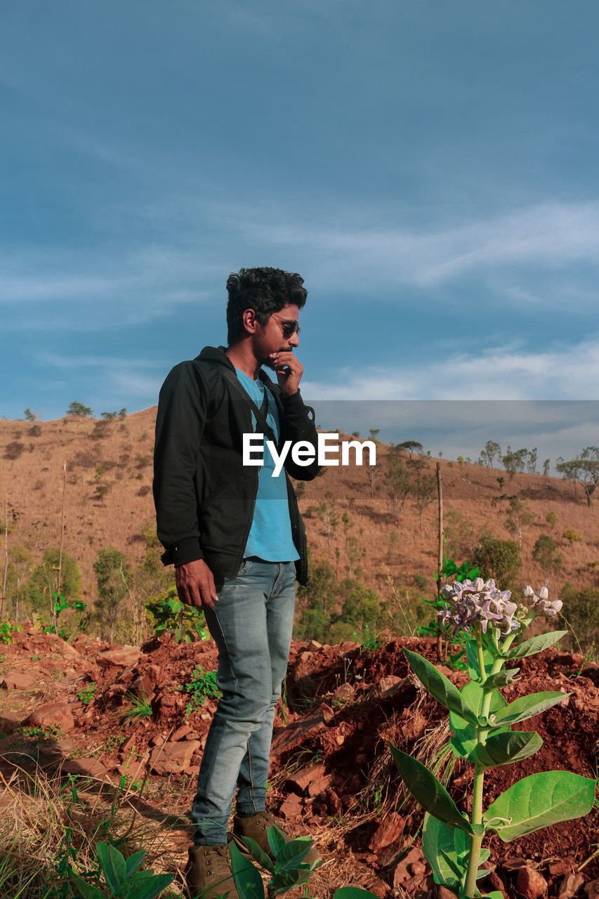 Full length of young man standing on land against cloudy sky