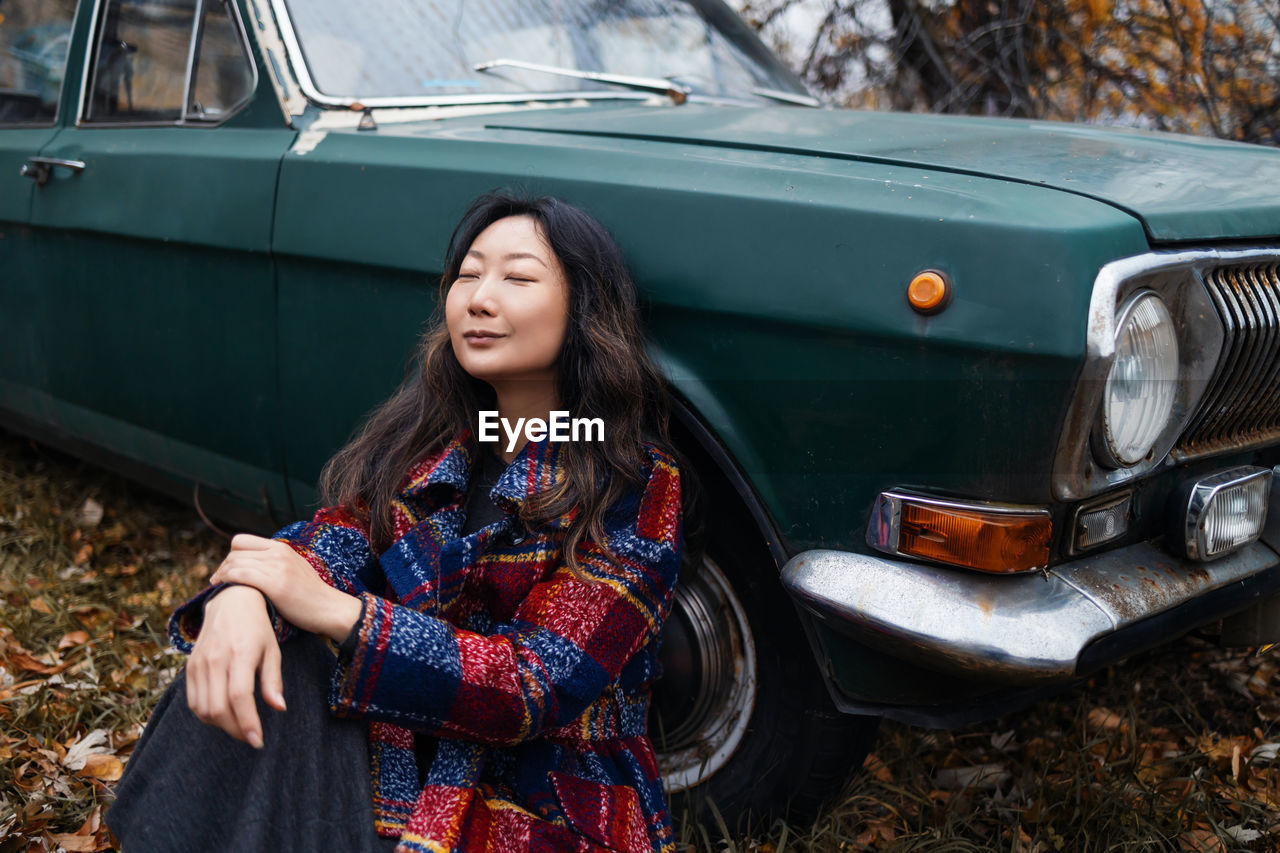 Portrait of smiling young asian woman near retro car