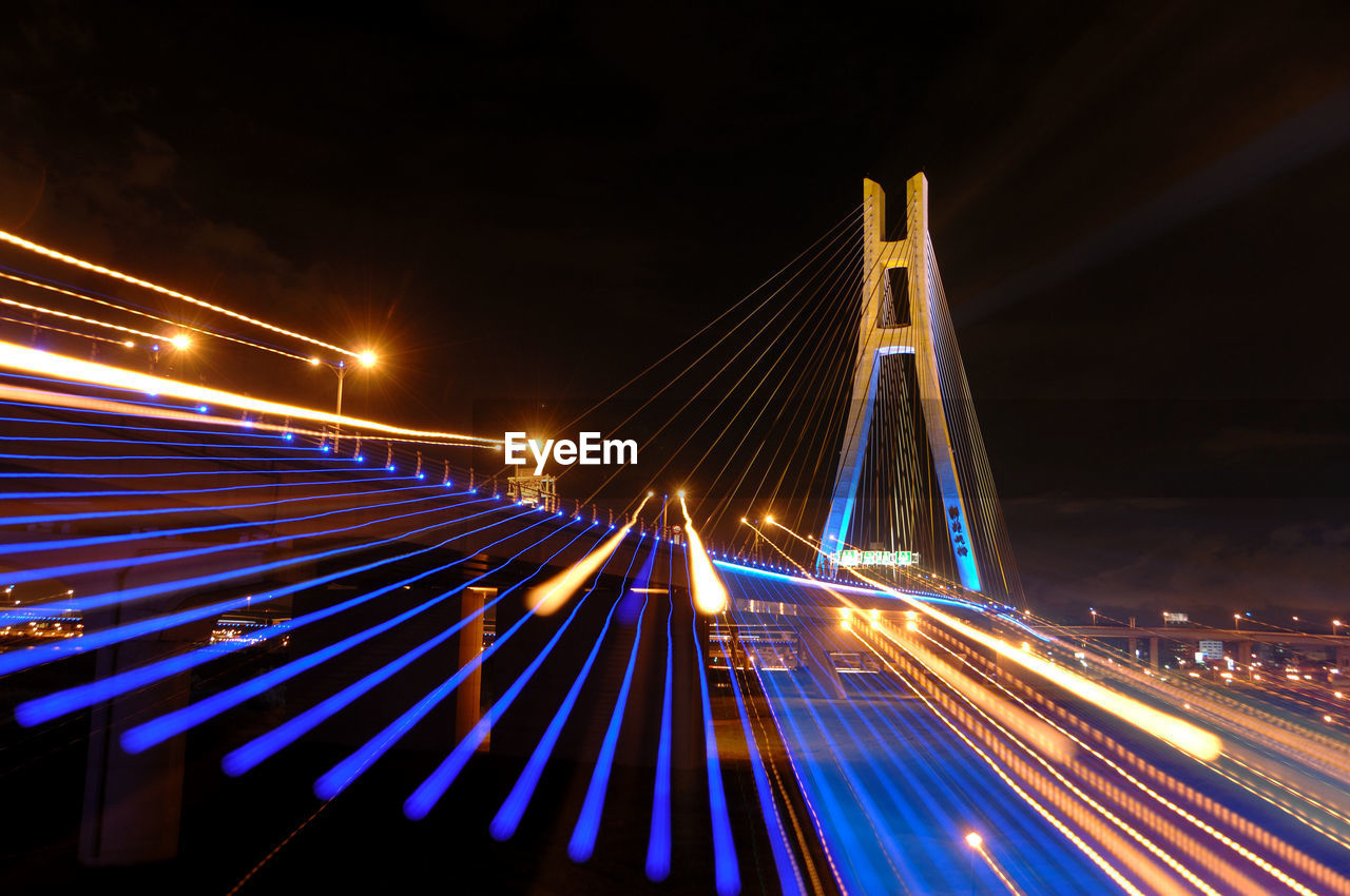 LIGHT TRAILS ON BRIDGE IN CITY AT NIGHT