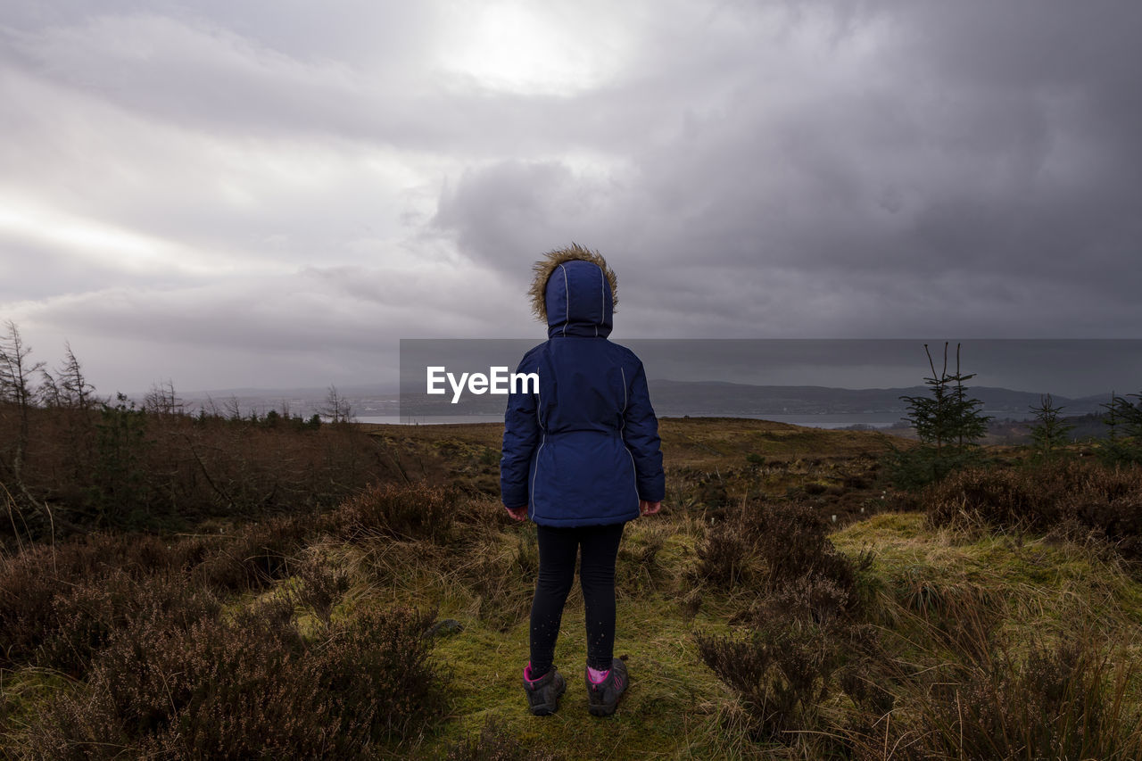 Rear view of girl standing on field against cloudy sky