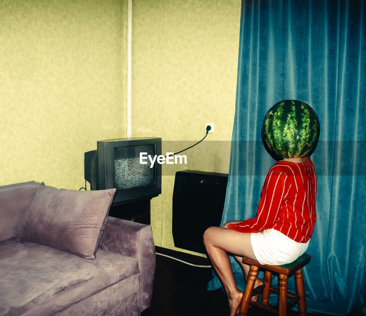 Young woman wearing watermelon on head sitting at home