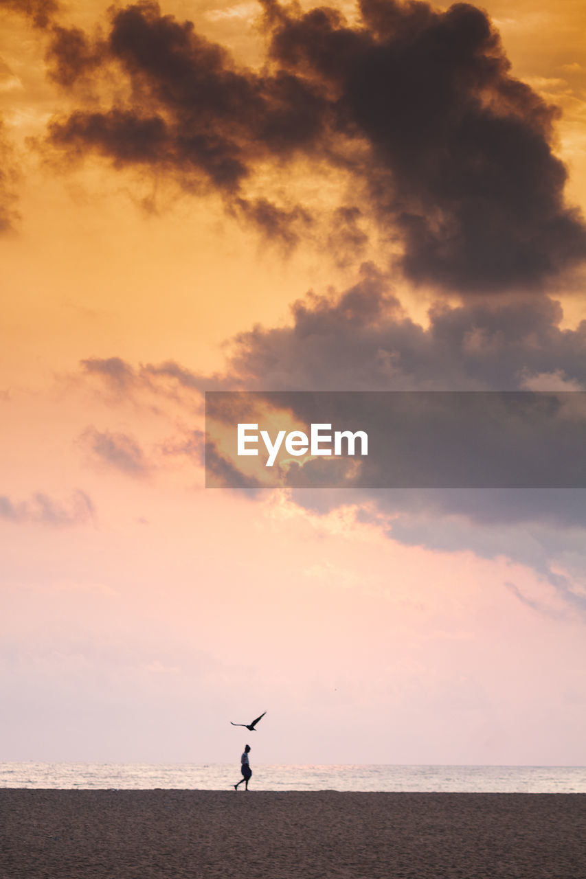 Woman walking at beach against sky during sunset