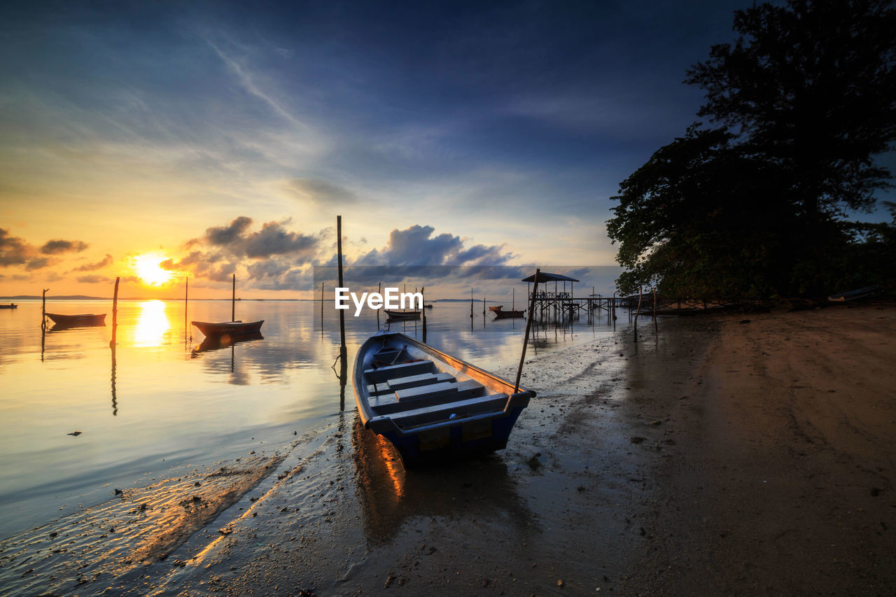 BOAT MOORED ON SHORE AGAINST SKY DURING SUNSET