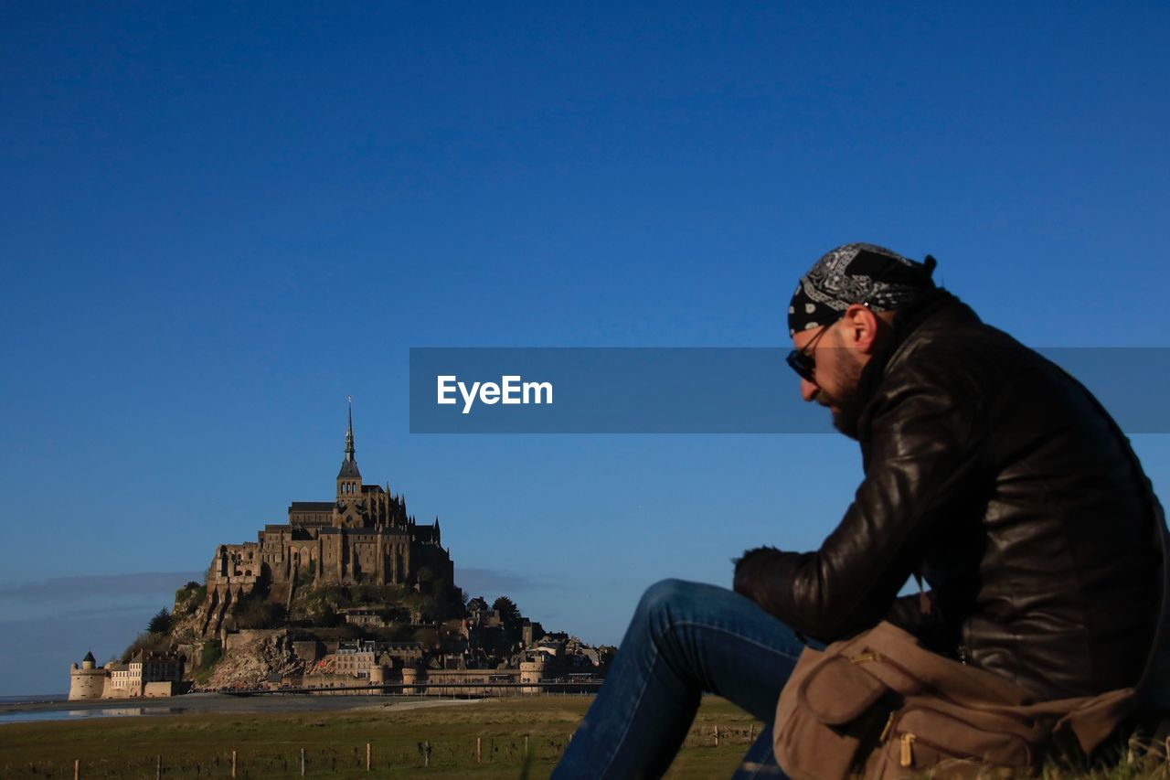 Side view of man sitting at mont saint-michel against clear sky