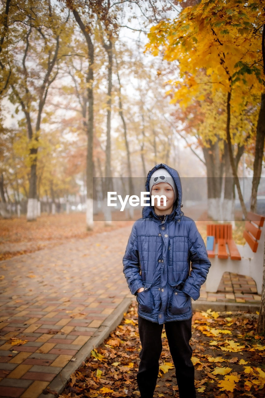 Portrait of boy standing by bench at park