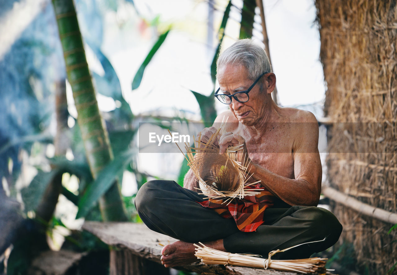 Senior man making craft product while sitting outdoors