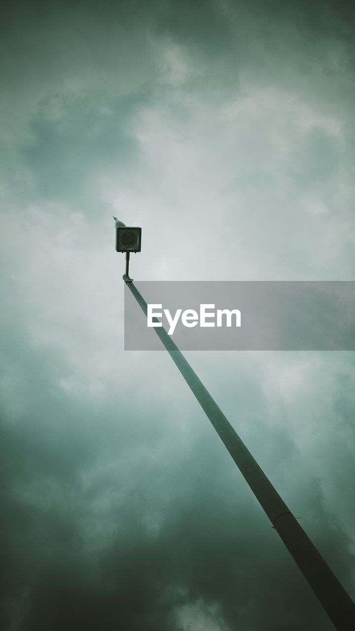 Low angle view of bird perching on street light against cloudy sky