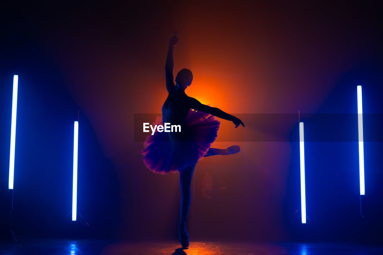 Silhouette of ballerina is practicing elements in studio with neon light. young woman dancing