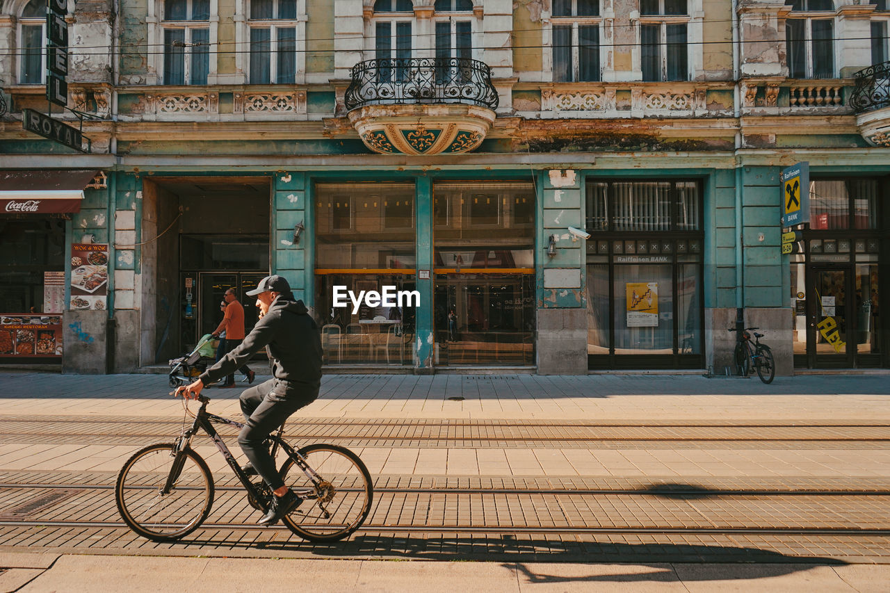 MAN RIDING BICYCLE ON STREET AGAINST BUILDING