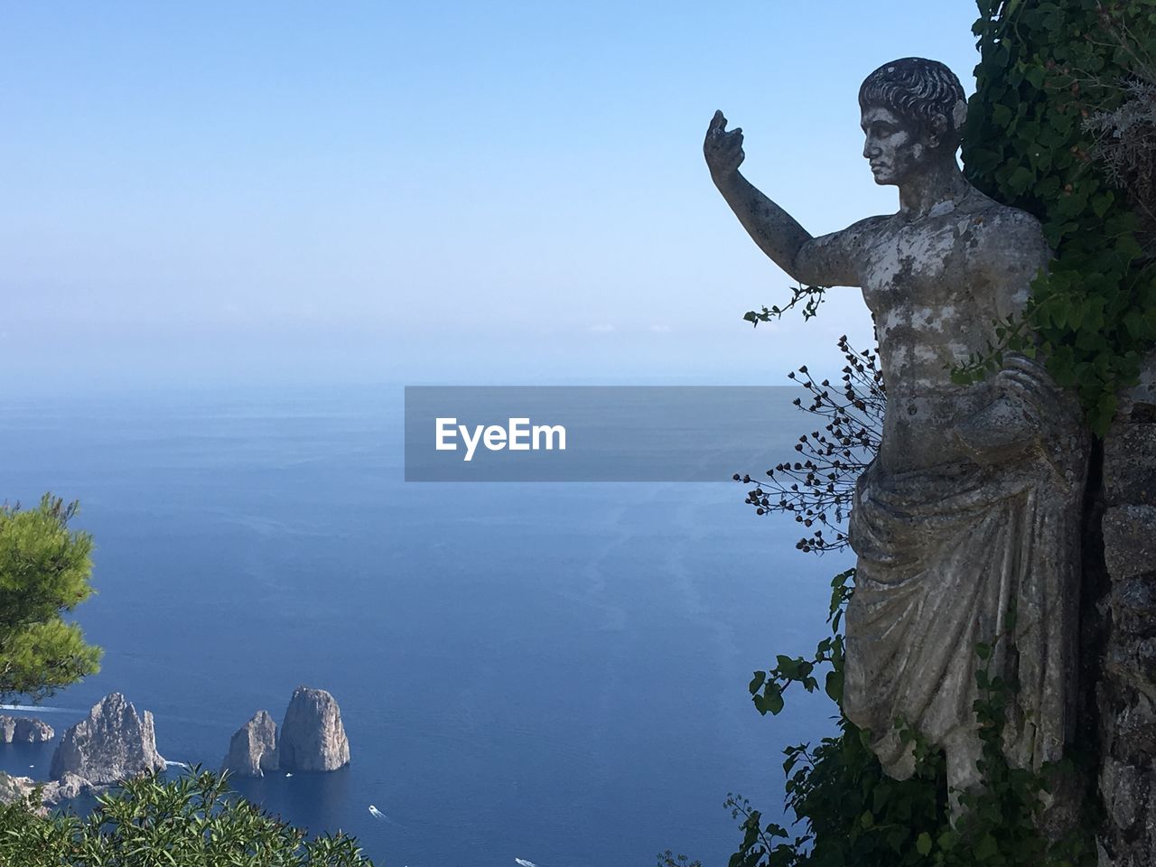 STATUE ON ROCK BY SEA AGAINST SKY