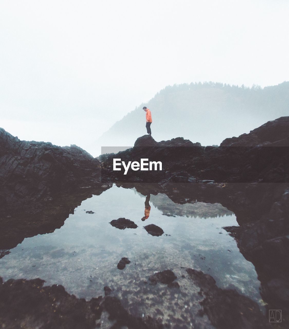 Man standing on rock by water against sky