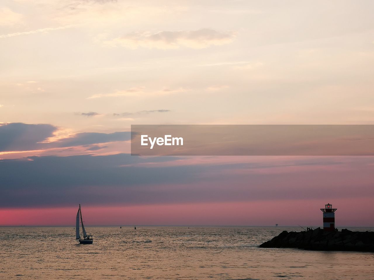 Lighthouse by sea against sky during sunset