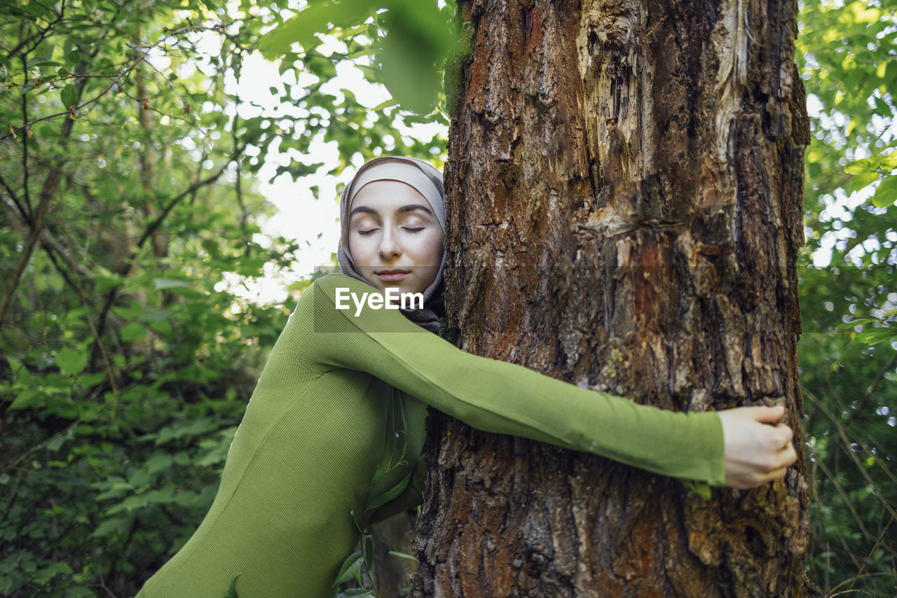 young woman standing against tree trunk