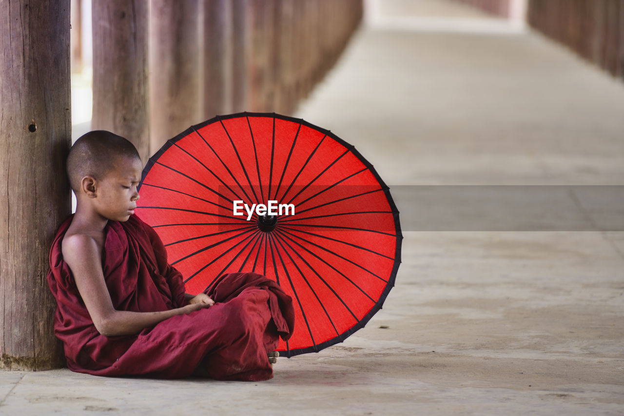 Monk with red umbrella sitting in temple