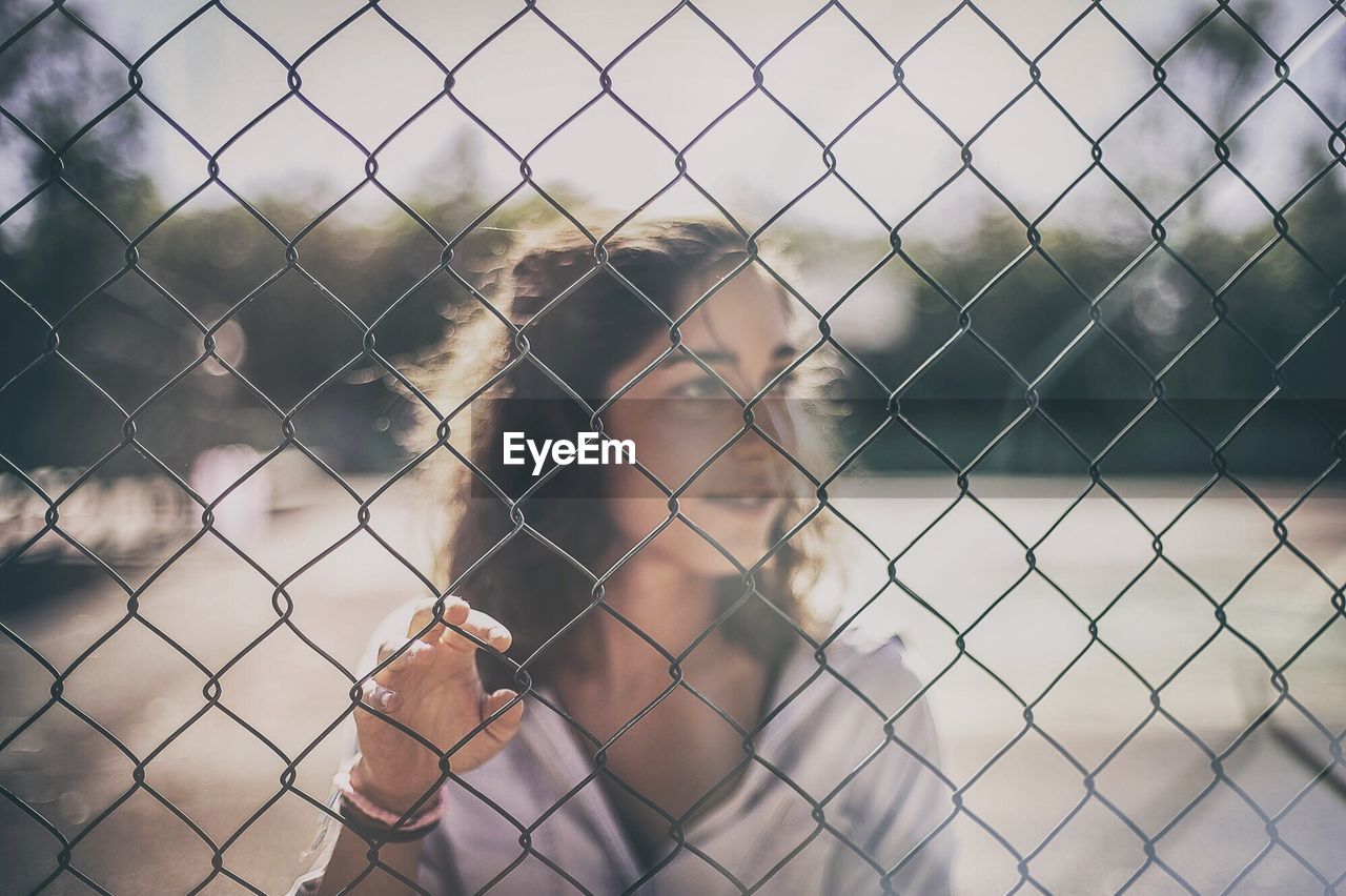 CLOSE-UP OF SHIRTLESS SEEN THROUGH CHAINLINK FENCE AGAINST SKY