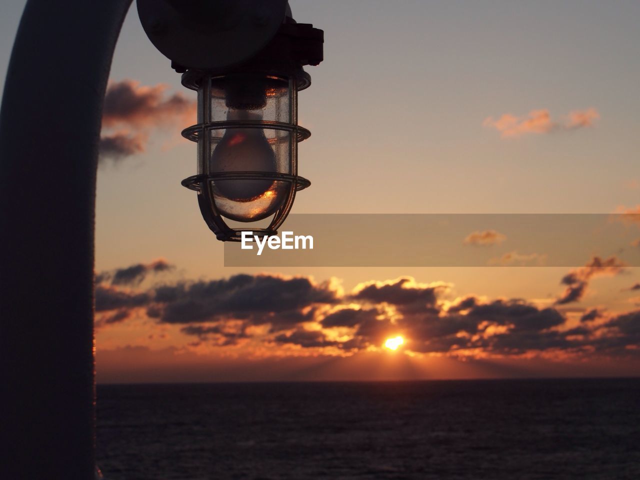 Street light by sea against orange sky