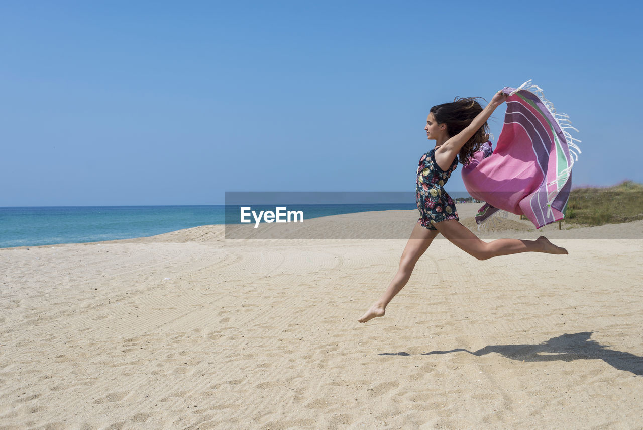 Full length of girl jumping with fabric at beach