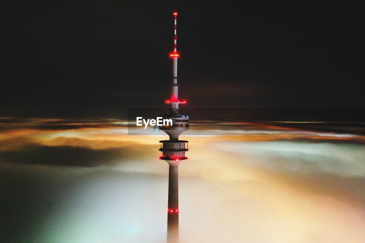 Communications tower in city against sky at night