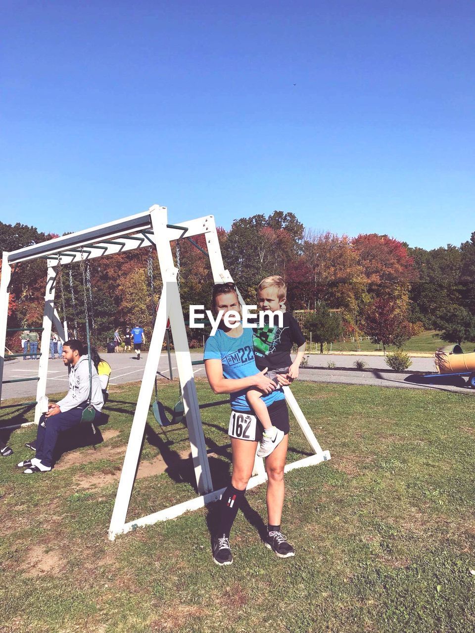 Mother carrying son at playground against clear sky